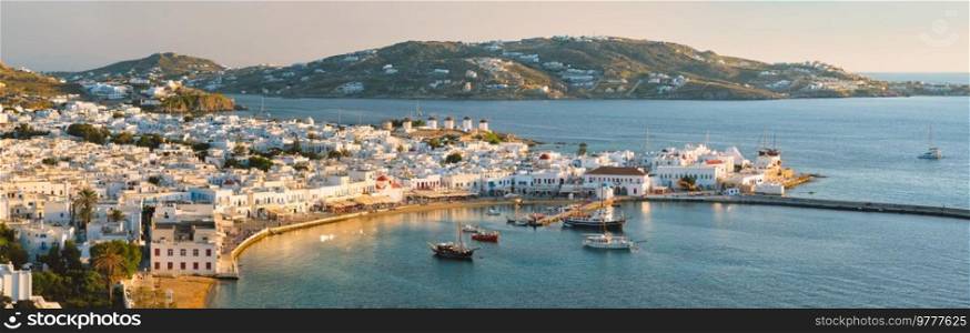 View of Mykonos town Greek tourist holiday vacation destination with famous windmills, and port with boats and yachtson sunset . Mykonos, Cyclades islands, Greece. With horizontal camera panning. Mykonos island port with boats, Cyclades islands, Greece