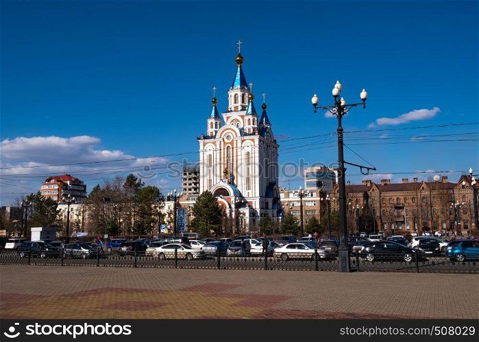 View of one of the streets of Khabarovsk in the daytime against a blue bright sky and white clouds. The combination of ancient architecture with modern buildings.. Khabarovsk, Russia - Apr, 27, 2019: Grado-Khabarovsk Cathedral of the Assumption of the Mother of God. Komsomolskaya square in the daytime with a bright blue sky with white clouds.