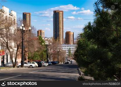 View of one of the streets of Khabarovsk in the daytime against a blue bright sky and white clouds. The combination of ancient architecture with modern buildings.. Khabarovsk, Russia - Apr, 27, 2019: The view of the Shevchenko street and Lenina street. Old houses combined with modern high-rise towers.