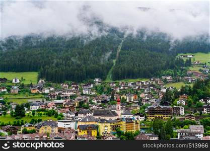 View of Ortisei Village in South Tyrol, Italy after rain with the rain clouds covered the mountain and forest of pine trees, the residential building and the church