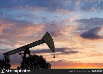 view of pumpjack pumping oil at summer sunset