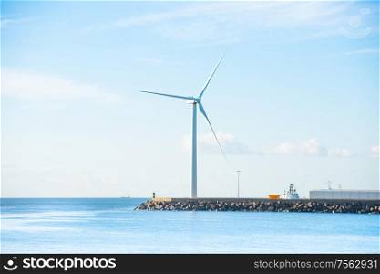 View of sea bay and large windmill at edge of stone breakwater