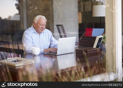 View Of Senior Man Using Laptop Through Window