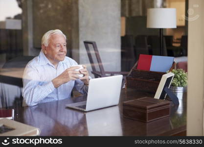 View Of Senior Man Using Laptop Through Window