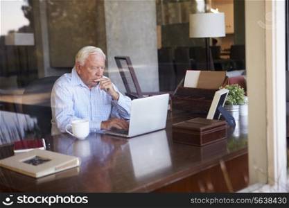 View Of Senior Man Using Laptop Through Window