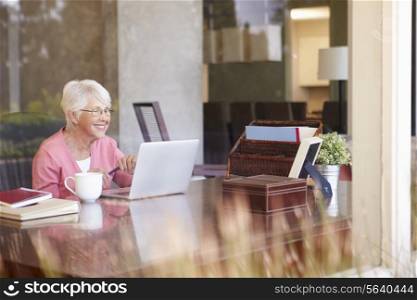 View Of Senior Woman Using Laptop Through Window