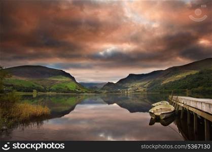 View of Snowdon covered in cloud at sunrise from Llyn Nantlle with reflections in lake and vibrant colors with rowing boats moored at jetty