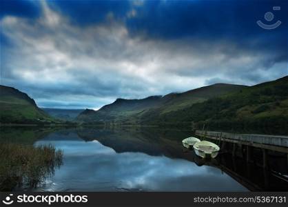 View of Snowdon covered in cloud at sunrise from Llyn Nantlle with reflections in lake and vibrant colors with rowing boats moored at jetty