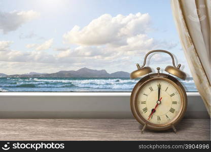 View of summer sea under blue sky from window with alarm clock