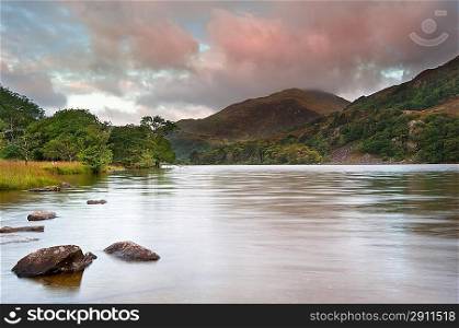 View of sunrise over Llyn Gwynant towards landscape of Yr Afan mountain in Snowdonia National Park