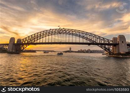 View of Sydney harbor bridge at sunset and a boat sailing under it in the background