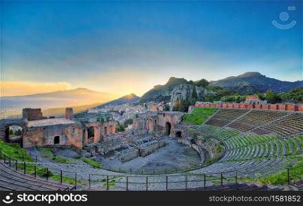 View of the ancient greek theater of Taormina with Etna volcano in eruption