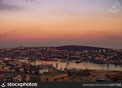 View of the city of Vladivostok from the hill eagle's nest . Sunset. The sky is orange and pink. Sea and city at sunset.. Panoramic view of the city of Vladivostok against the sunset.