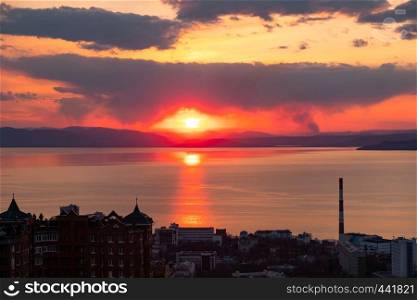 View of the city of Vladivostok from the hill eagle's nest . Sunset. The sky is orange and pink. Sea and city at sunset.. Panoramic view of the city of Vladivostok against the sunset.