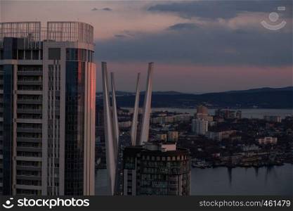 View of the city of Vladivostok from the hill eagle's nest . Sunset. The sky is orange and pink. Sea and city at sunset.. Panoramic view of the city of Vladivostok against the sunset.