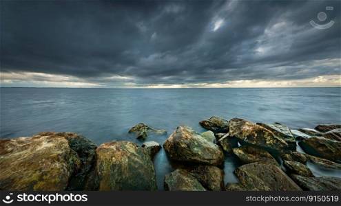View of the lake from the boulders shore with impending rain and storm clouds at IJsselmeer Netherlands near the village Urk in Flevoland. Raging cloudy skies above lake along coastal shore