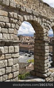 View of the old town through an arch of the roman aqueduct in Segovia, Spain