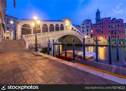 View of the Rialto Bridge and Grand Canal in a night lighthouse at sunset. Venice. Italy.. Venice. Rialto Bridge at sunset.