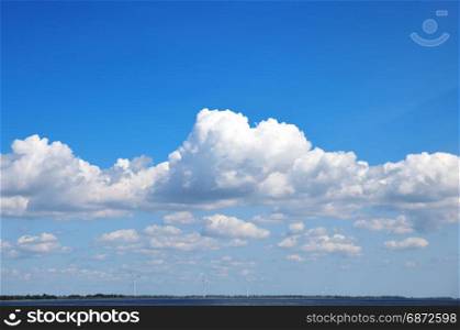 view of the sea with windmills in the distance, a blue sky with white fluffy clouds