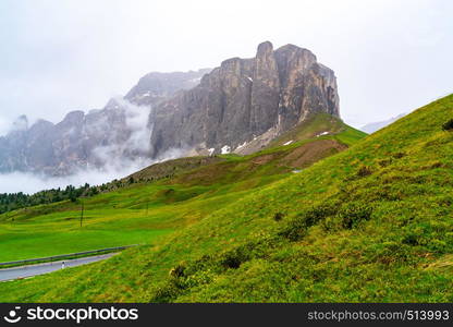 View of the Sella Group Mountain range after rain at the Sella Pass in Italy with the field of green grass and the hill of yellow flowers