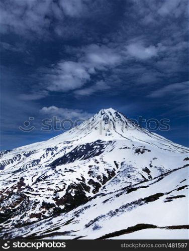 View of the snowy volcano Vilyuchinsky and blue sky with clouds in spring in Kamchatka