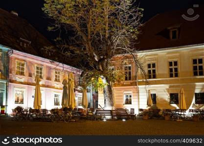 view of the street cafe on the main square in the historic city center Sighisoara illuminated by the street lamps.