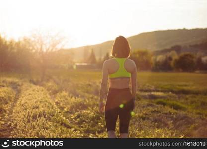 View of woman from behind with sportswear, walking on country road, portrait
