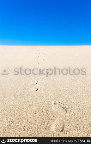 View of yellow sand, blue sky and footsteps disappearing into the distance. Vertical photo of an empty beach.. View of yellow sand, blue sky and footsteps disappearing into the distance. Vertical photo of an empty beach