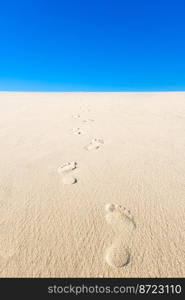 View of yellow sand, blue sky and footsteps disappearing into the distance. Vertical photo of an empty beach.. View of yellow sand, blue sky and footsteps disappearing into the distance. Vertical photo of an empty beach