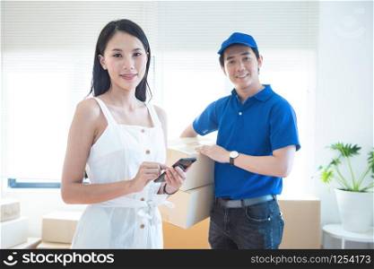 View of young asian woman appending signature in digital smart mobile phone after receiving parcel from courier delivery man at home.AI Technology transportation concept.