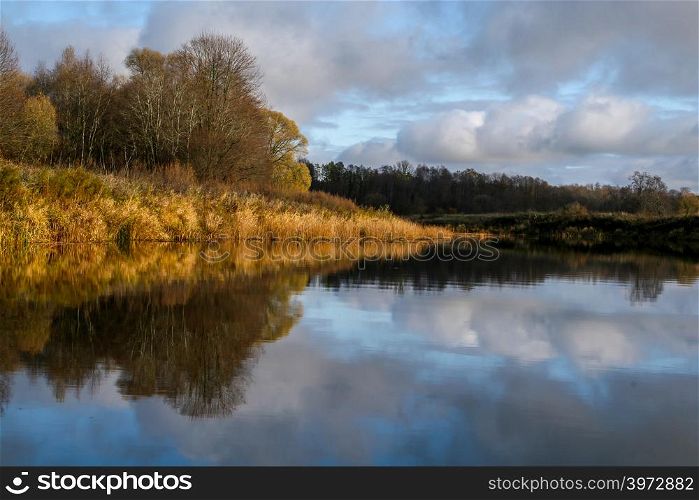 View on autumn landscape of river and trees in sunny day. Forest on river coast in autumn day. Reflection of autumn trees in water. Autumn in Latvia. Autumn landscape with colorful trees and river.