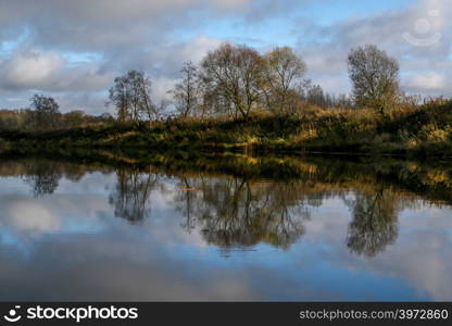 View on autumn summer of river and trees in sunny day. Forest on river coast in autumn day. Reflection of autumn trees in water. Summer in Latvia. Autumn landscape with colorful trees and river.