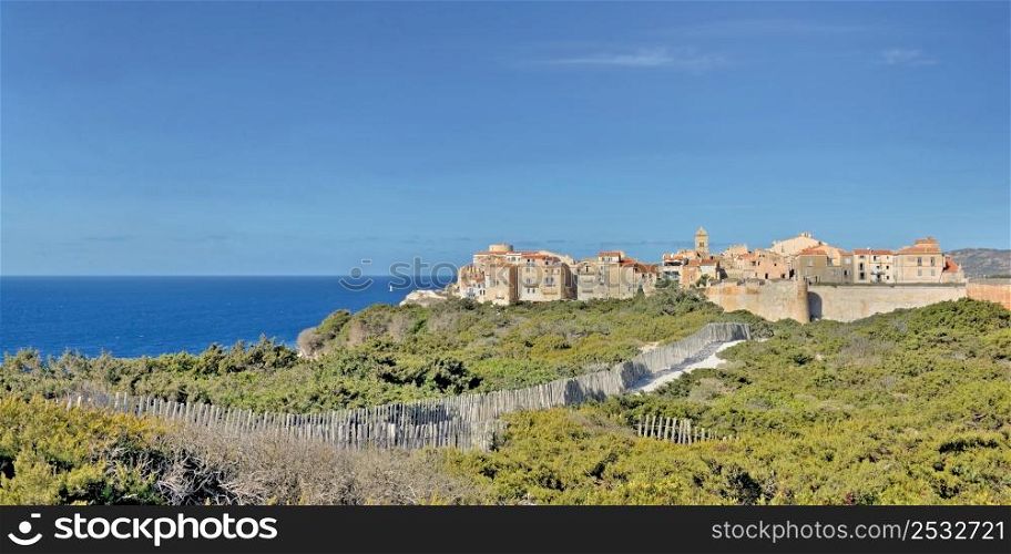 view on famous fortress at Bonifacio in Corsica from path in bush under blue sky