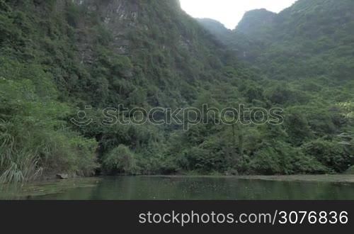 View on mountain with trees and dark cave from lake. Approach by boat in still water. National park Phong Nha-Ke Bang, Vietnam
