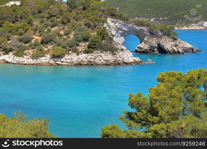view on natural arch formed in the cliff in a turquoise blue sea in the park Gargano - Puglia Italy	