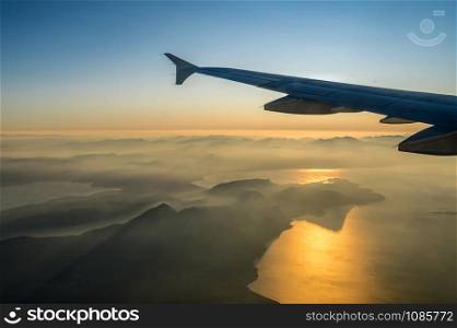 View on passenger aircraft left wing. Sun shines as a light beam over the wing. Thick clouds below airplane are illuminated by the. Golden sun. Horizontal view