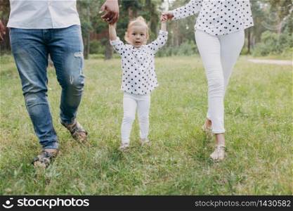 View on toddler. Mother, father hold hands daughter walk in the forest. Young family spending time together on vacation, outdoors. The concept of family summer holiday. selective focus.. View on toddler. Mother, father hold hands daughter walk in the forest. Young family spending time together on vacation, outdoors. The concept of family summer holiday. selective focus