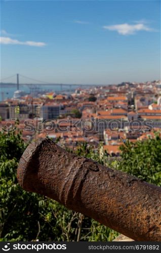 view on travel city Lisbon with old metal cannon trunk from top place of castle sao jorge. roofs, river tejo, brige 25 april, ships in summer day.