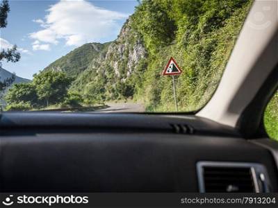 View on warning of landslide sign on road from inside of car at sunny day