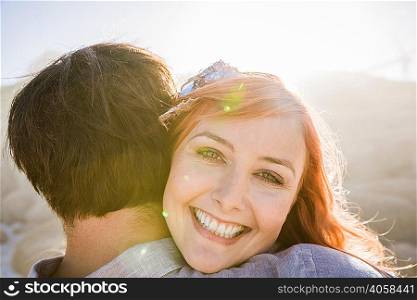 View over shoulder of woman hugging man, looking at camera smiling
