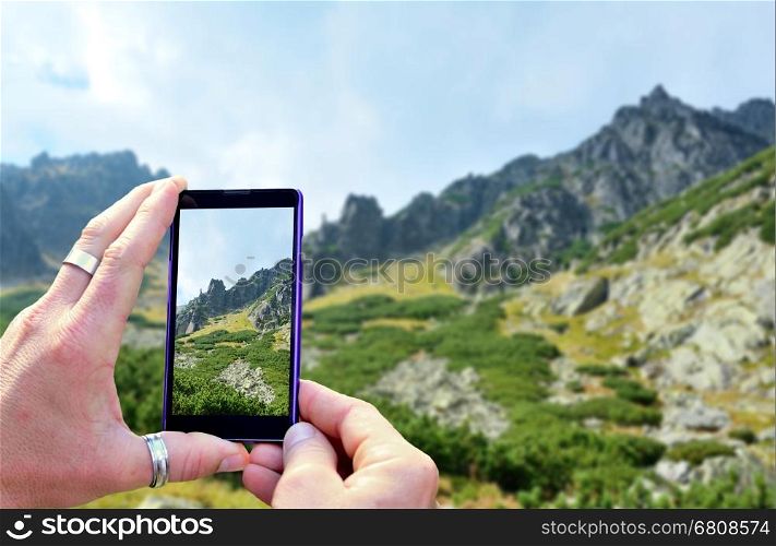 View over the mobile phone display during taking a picture of landscape in nature. Holding the mobile phone in hands and taking a photo. Focused on mobile phone screen.