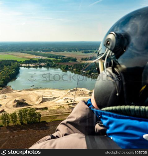 View over the shoulder of the pilot of a gyrocopter during a flight over a gravel pond in the North German heath landscape.