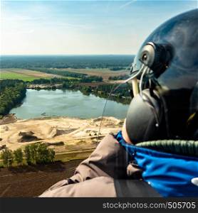 View over the shoulder of the pilot of a gyrocopter during a flight over a gravel pond in the North German heath landscape.