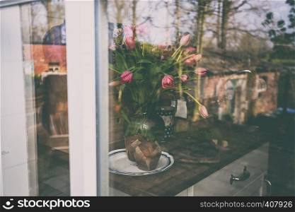 view through a windowpane on a vase with pink tulips and cupcakes