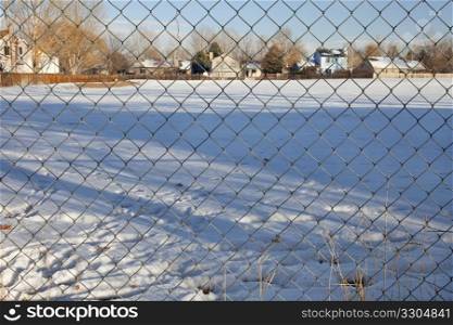 view through chain link fence on a typical residential neighborhood in Fort Collins, Colorado; winter scenery with long tree shadows