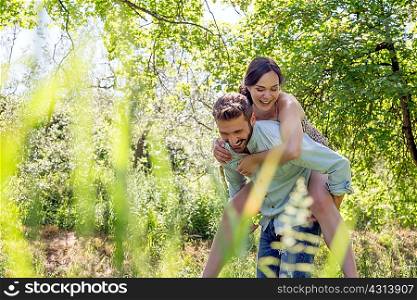 View through foliage of young man giving young woman piggyback