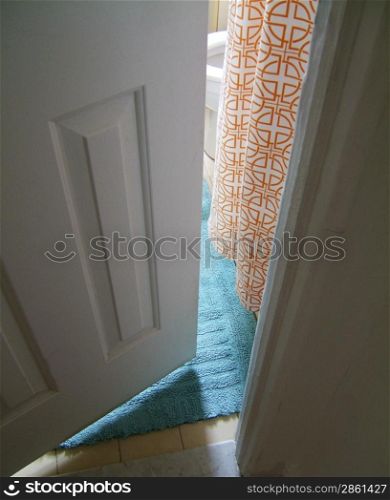 View through narrowly open door onto a blue rug and orange detailed curtain
