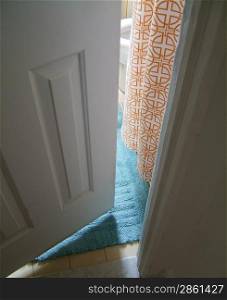 View through narrowly open door onto a blue rug and orange detailed curtain