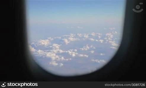 View through the plane illuminator to beautiful white heap clouds over the land. Air travel