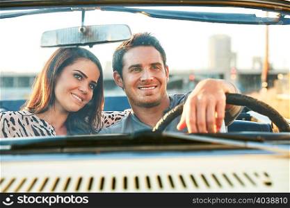 View through windscreen of couple in convertible car smiling, Los Angeles, California, USA